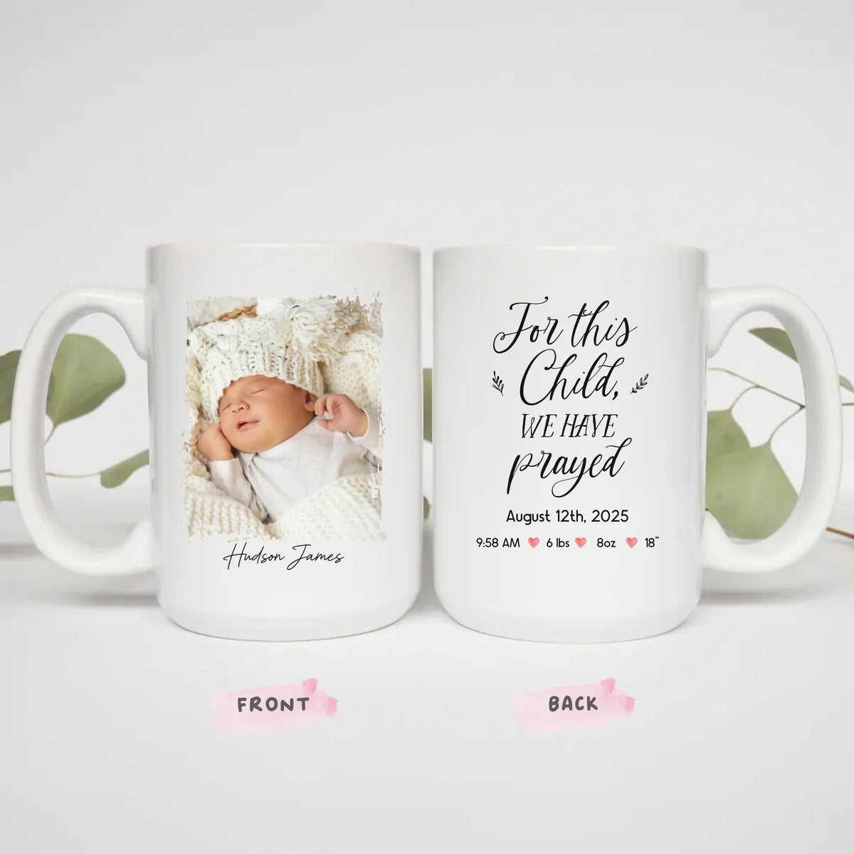 Two 15oz For This Child We Prayed mugs styled with eucalyptus greenery